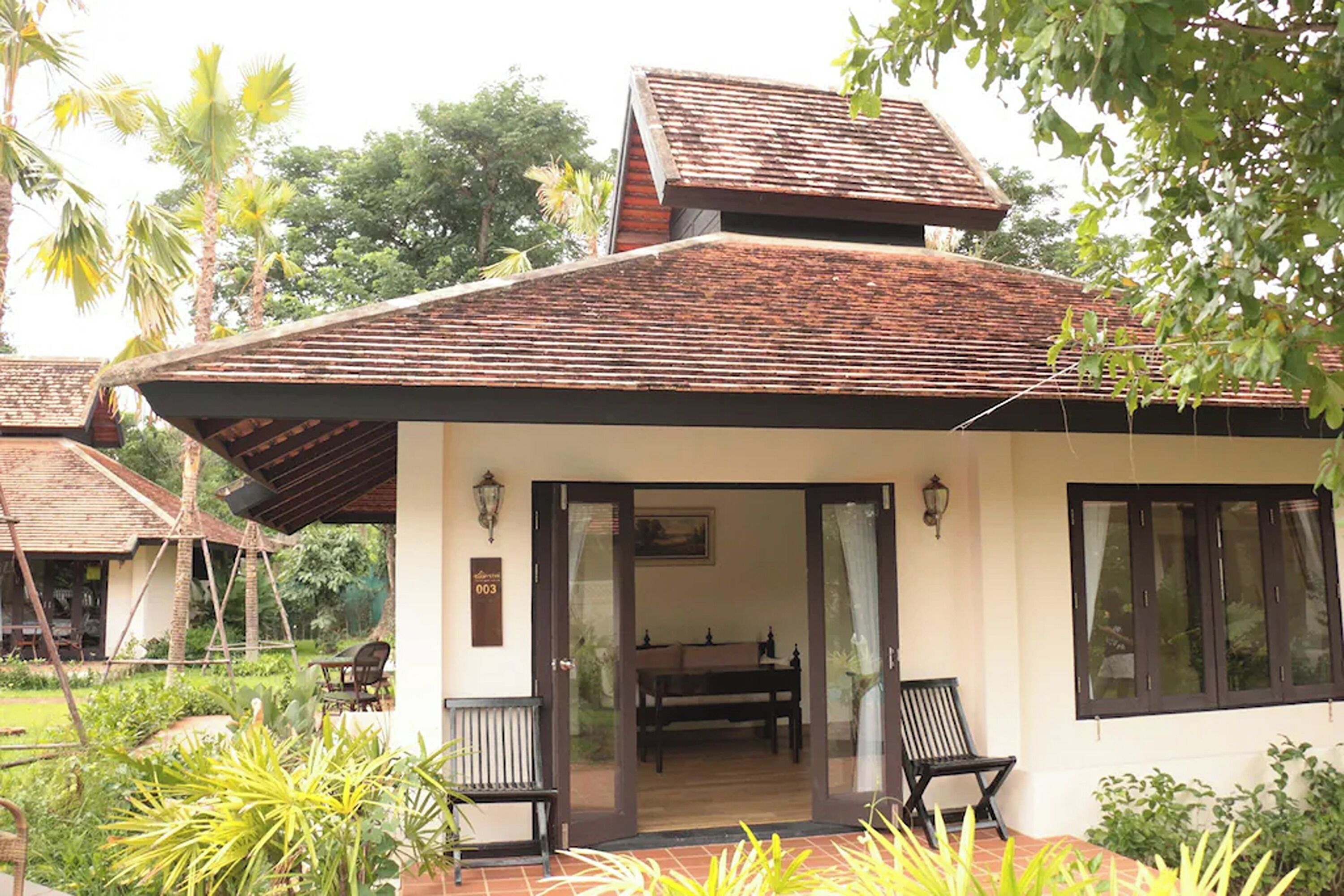 A bungalow with a tiled roof, a covered porch, and a dining area with a table and chairs.
