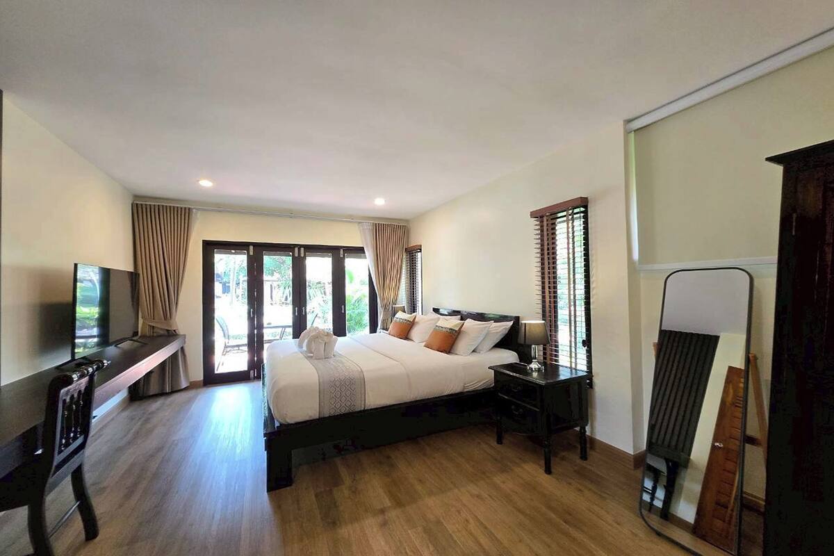 A hotel room with a bed, a desk, a TV, a mirror, and a window with curtains.