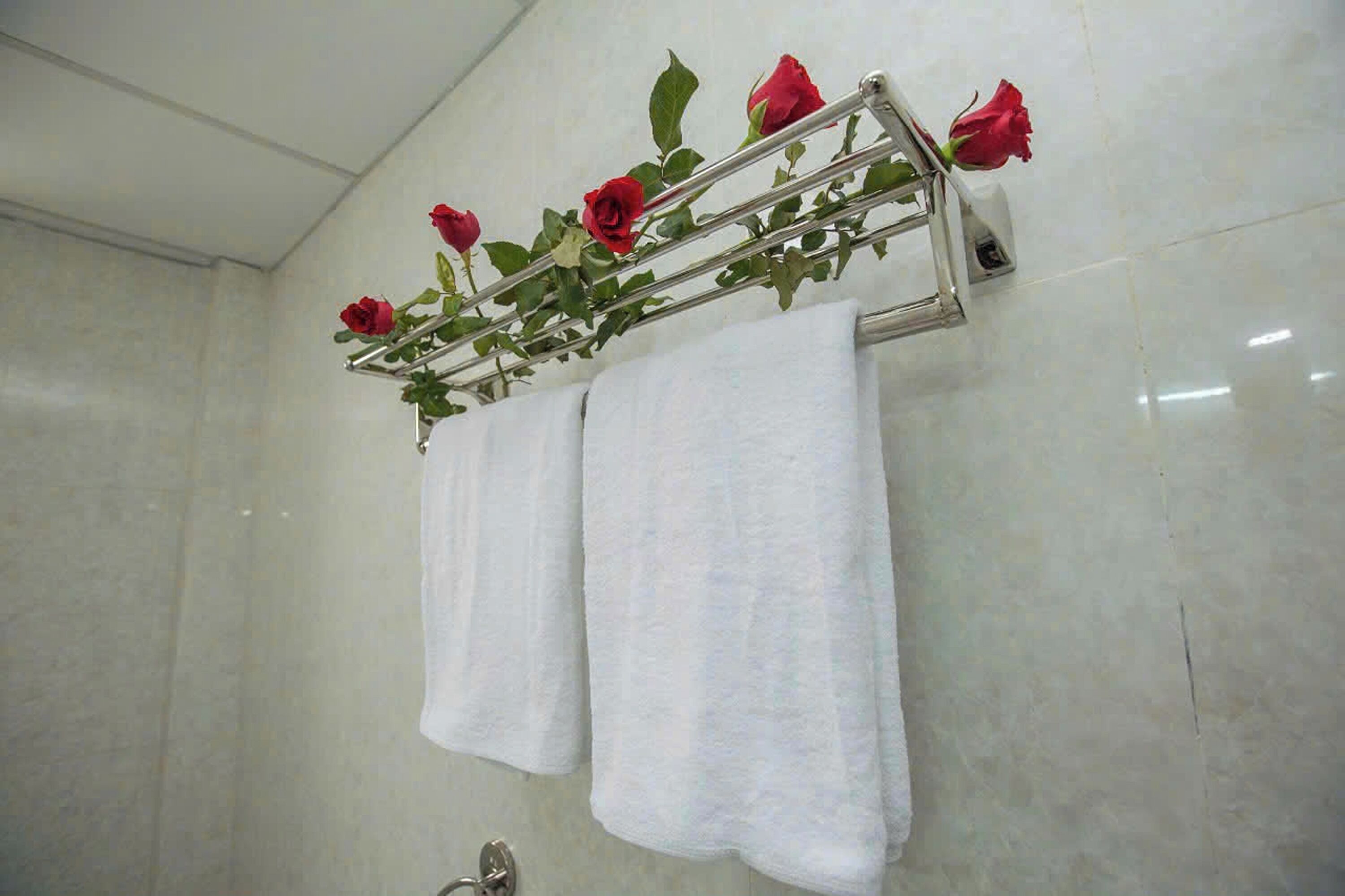 Een badkamer met een metalen handdoekhouder met verschillende rode rozen en twee witte handdoeken.