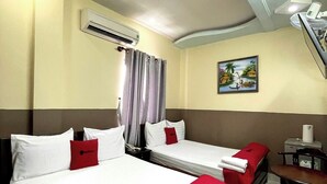 Ein Hotelzimmer mit zwei Betten, einem Schreibtisch, einem Stuhl, einer Klimaanlage und einem Bild an der Wand.