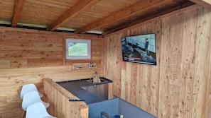 Ein Holzhütten-Innenraum mit Holzboden, einem kleinen Fenster, einem Waschbecken und einem an der Wand befestigten Fernseher.
