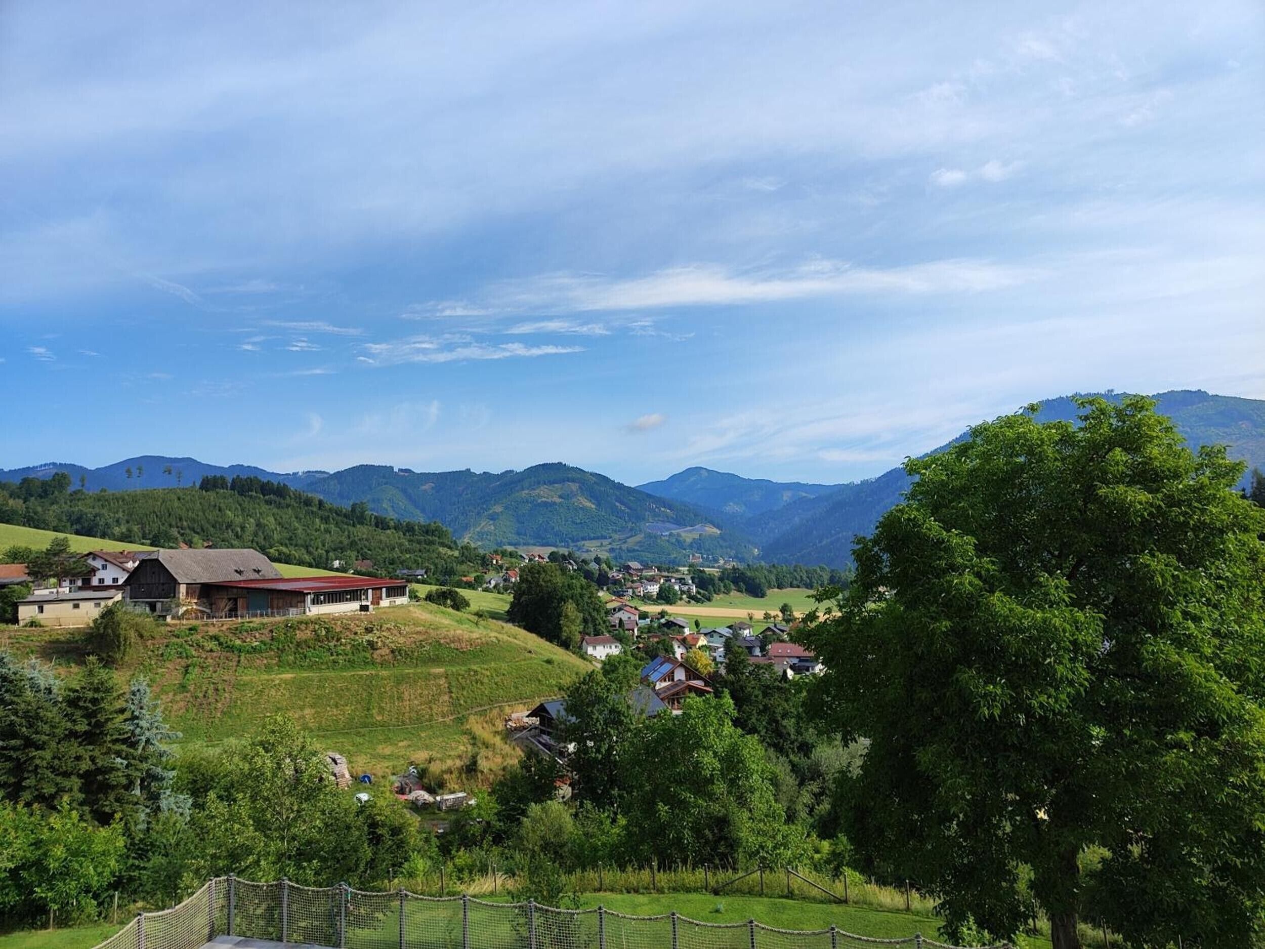 Un paysage rural avec des maisons, une zone délimitée par une clôture et des montagnes en arrière-plan.