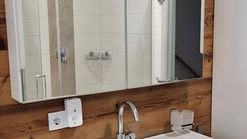 A bathroom with a large mirror, a white sink, and a shower enclosure.