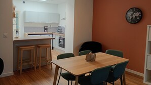 A modern kitchen with white cabinets, a built-in oven, and a coffee maker. There is a dining area with a wooden table and four chairs. - Maison 5 ch Wifi Exterieur (Faches-Thumesnil)