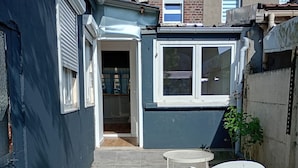 A narrow courtyard with a tiled floor, a white plastic chair, a small round table, and a white plastic sofa. - Maison 5 ch Wifi Exterieur (Faches-Thumesnil)