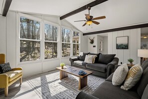 A living room with large windows, a ceiling fan, a sofa, a coffee table, and a patterned rug. - Pocono Cabin + Deck + Firepit | Near Big Boulder & Jack Frost | Estates Drive (Lake Harmony)