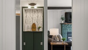 Una stanza con una porta verde, uno scaffale a parete con oggetti decorativi, un televisore e un piccolo tavolo con una lampada.