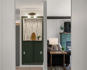 Ein Zimmer mit grüner Tür, einer an der Wand befestigten Ablage mit Dekoration, einem Fernseher und einem kleinen Tisch mit Lampe.