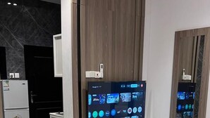 Una habitación de hotel moderna con una cama grande, un televisor de pantalla plana montado en la pared, un armario de madera y una pequeña kitchenette.