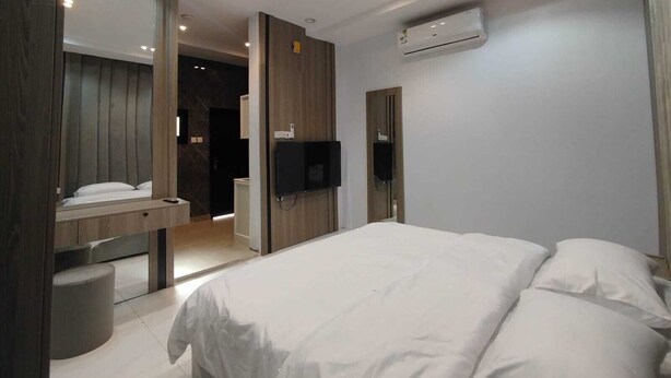Una habitación de hotel moderna con una cama, televisor, espejo y equipo de aire acondicionado.
