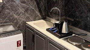 Una cocina con paredes de mármol, armarios grises, un fregadero, una tetera y un dispensador de agua.