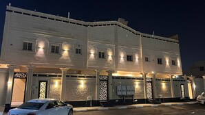 Un edificio de varios pisos con fachada simétrica, puertas de entrada iluminadas y un coche estacionado frente a él.