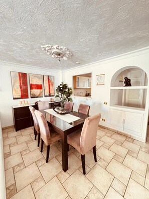 A dining room with a dark wooden table, six chairs, a chandelier, and a kitchen area in the background. - Spacious 2-bedroom apartment with heated pool, close to the beach (Los Cristianos)