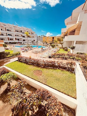 A hotel courtyard with a swimming pool, lounge chairs, and a well-maintained garden. - Spacious 2-bedroom apartment with heated pool, close to the beach (Los Cristianos)