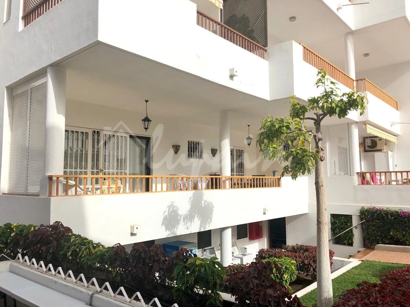 A multi-story building with balconies, a covered outdoor area, and a garden with various plants.