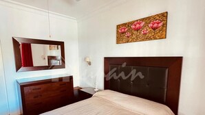 Une chambre à coucher comprenant un lit, un ventilateur de plafond, une table de chevet, une commode, un miroir et un tableau.