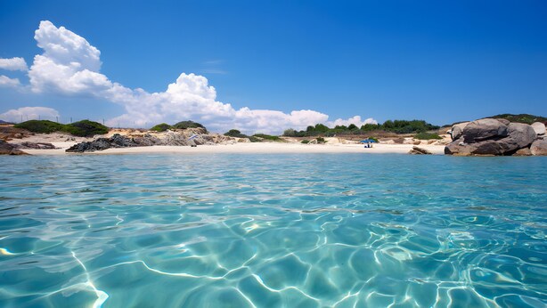 Een strand met helder water, een zandstrand en rotsformaties.