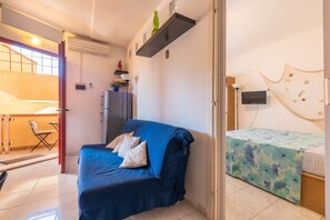 A compact room with a sofa, a bed with a floral bedspread, a TV, and a shelf with decorative items. - Casa Livia in the Heart of Villasimius (Villasimius)