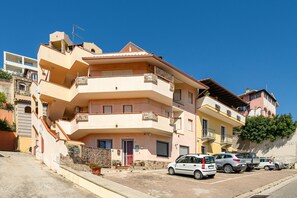 A multi-story residential building with balconies, a parking area with several cars, and a clear blue sky. - Casa Livia in the Heart of Villasimius (Villasimius)