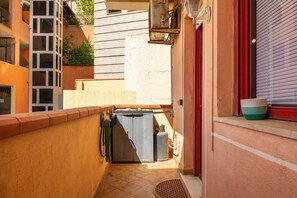 Un estrecho pasillo exterior con una reja metálica, un calentador de agua y una ventana con persiana.