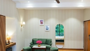 A room with a green sofa, a small table with a vase, a mirror, and a window with a view of greenery. - asar Suites GK1 By Orion Hotels (New Delhi)