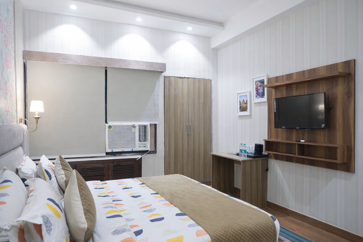 A hotel room with a bed, a desk, a TV, and an air conditioning unit.