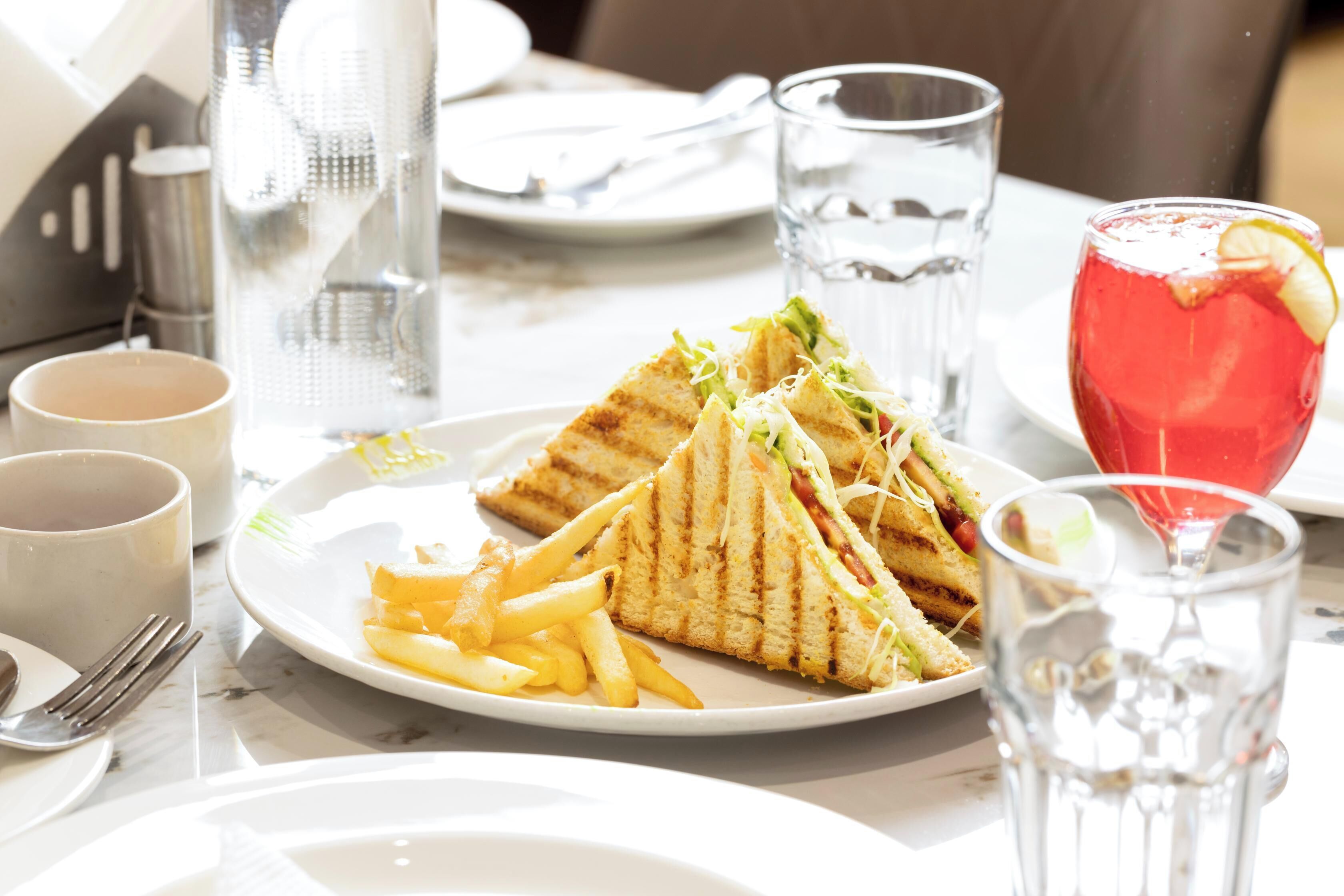 Un repas composé de sandwichs grillés, de frites et d’une boisson rouge, le tout servi dans une assiette blanche.