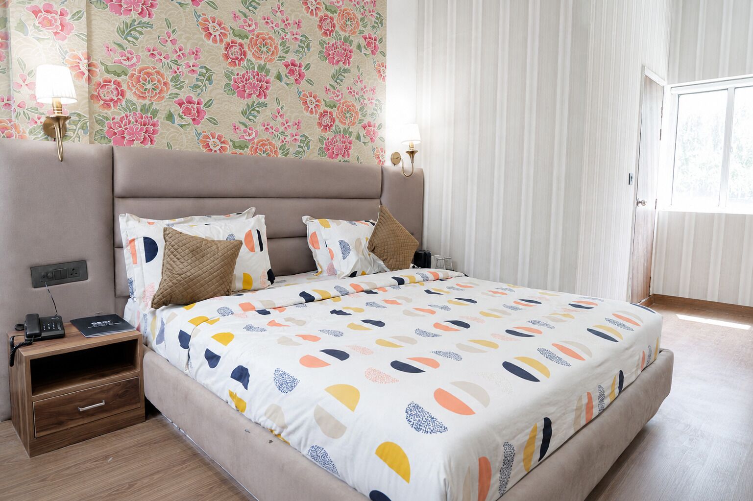 Une chambre à coucher avec un lit, des tables de chevet, des lampes, une commode et un papier peint à motifs floraux.