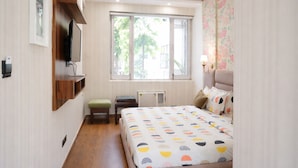 A bedroom with a bed, a TV mounted on the wall, a window, a ceiling fan, and a radiator. - asar Suites GK1 By Orion Hotels (New Delhi)