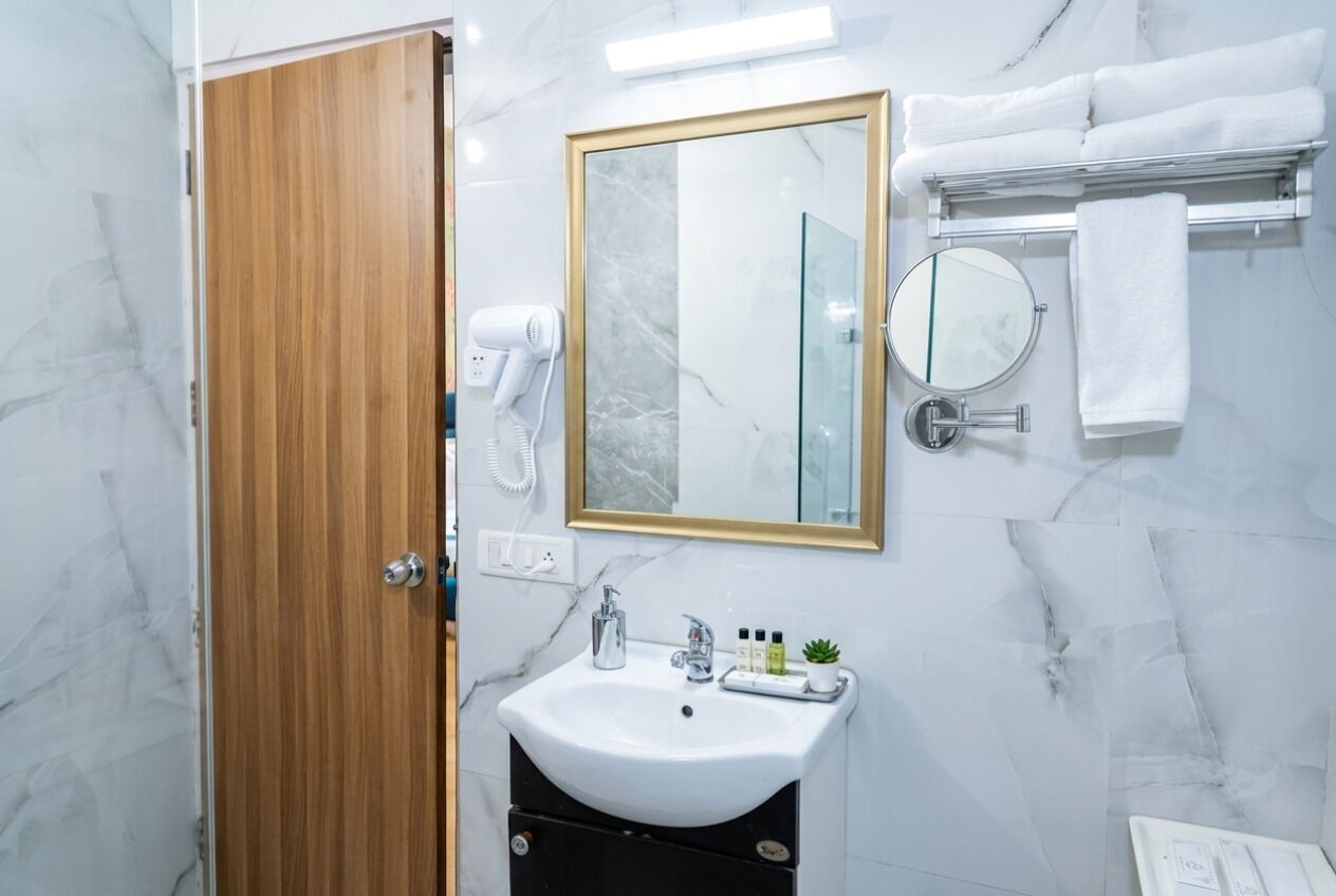A bathroom with a marble wall, a wooden door, a white sink, a mirror, a towel rack, and a hairdryer.