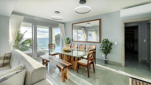 Ein moderner Essbereich mit einem Glastisch, Holzsesseln und Blick aufs Meer.