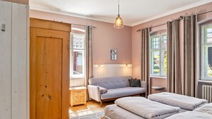 Une chambre à coucher comprenant un lit, un canapé, une armoire en bois, une petite table et une fenêtre avec des rideaux.