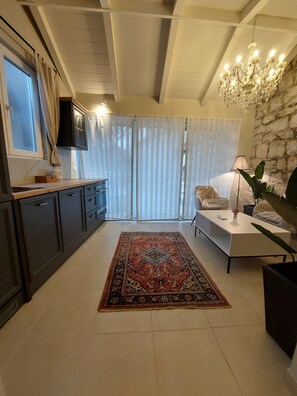 Ein modernes Wohnzimmer mit einer Küche, einer Kristallleuchtre, einem großen Teppich und einer Steinwand.