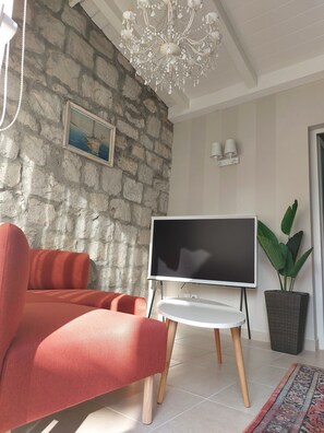 Ein Wohnzimmer mit Steinwand, einer Kristallleuchter, einem Flachbildfernseher, roten Sesseln, einem Topfpflanzen und einem gemusterten Teppich.