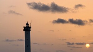 Et fyrtårns silhuet mod en solnedgangshimmel med skyer.
