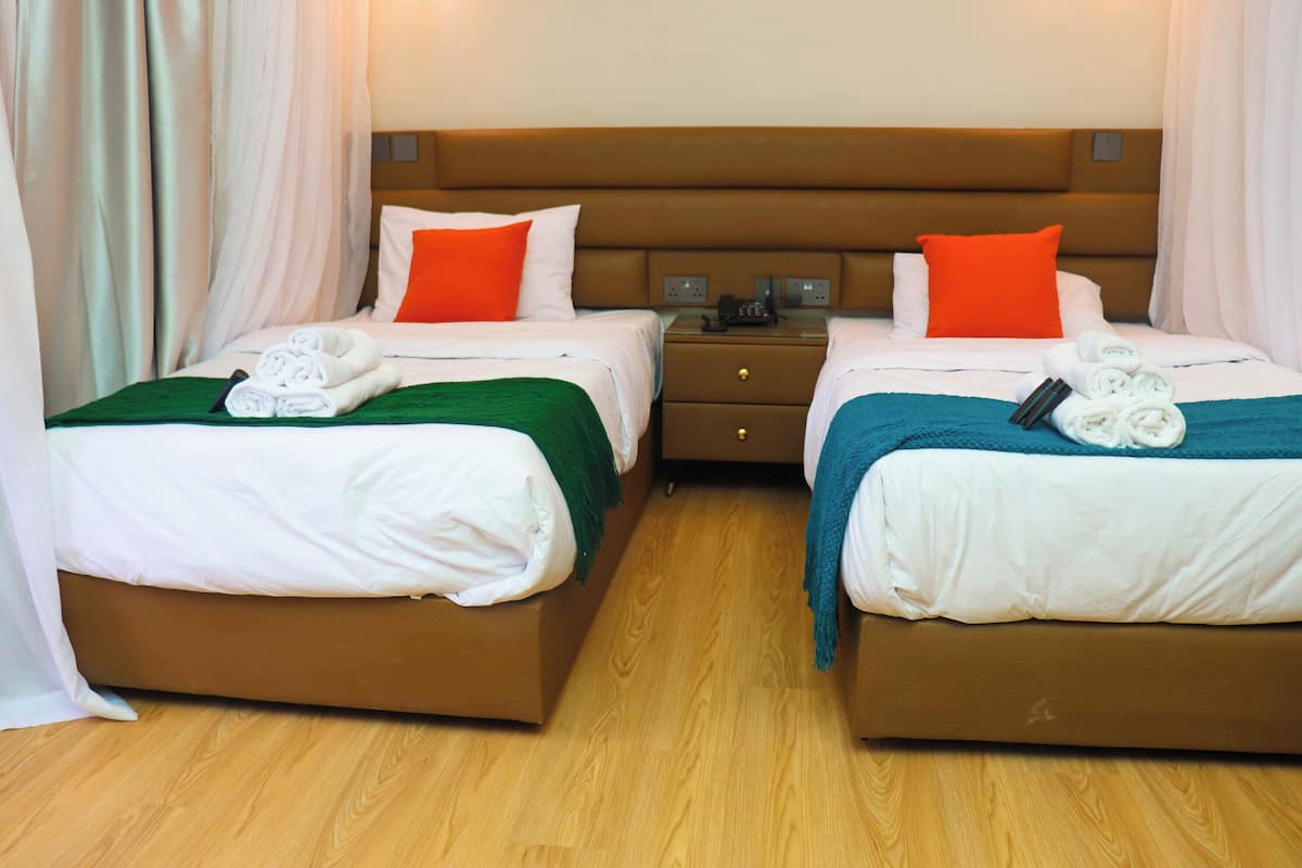 A hotel room with two beds, each with a pillow, a bedside table, and a lamp.