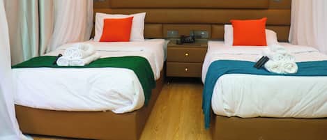 Habitación de hotel con dos camas, cada una con una almohada, una mesita de noche y una lámpara.
