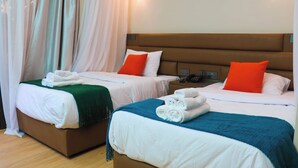 Two twin beds with white bedding and orange pillows, a green throw blanket on one bed, and a brown headboard.