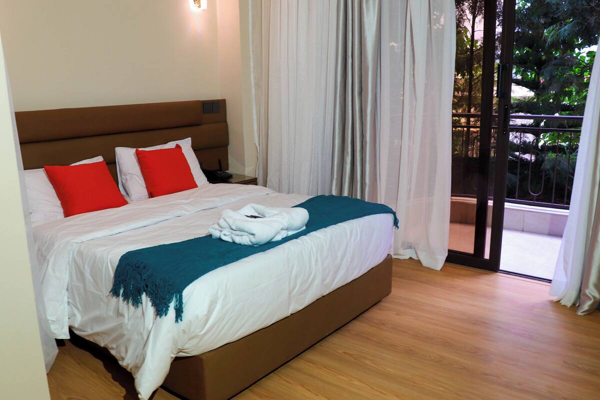 A bedroom with a bed, curtains, and a view of the outdoors.