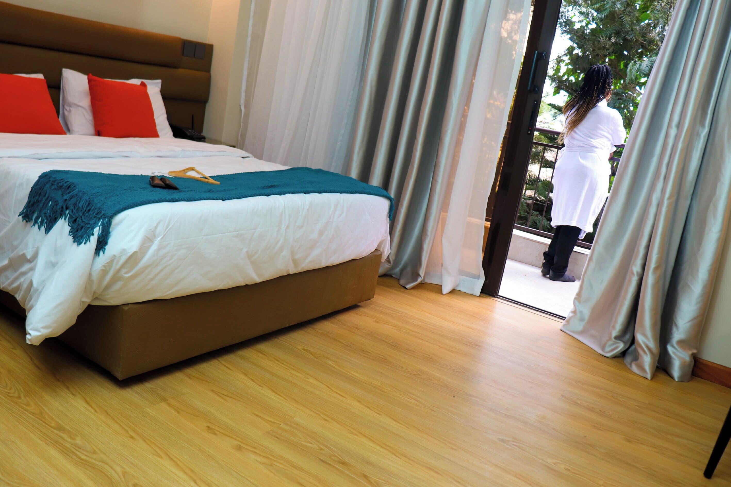 Habitación de hotel con una cama grande, piso de madera y vistas a través de un ventanal.