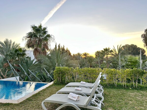 A poolside area with lounge chairs, a pool, and surrounding greenery.
