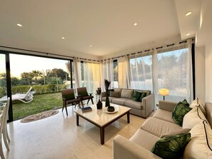 A modern living room with a sofa, chairs, a coffee table, and a view of a garden through large windows.