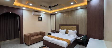 A modern hotel room with a large bed, a sofa, a desk, and a ceiling fan.