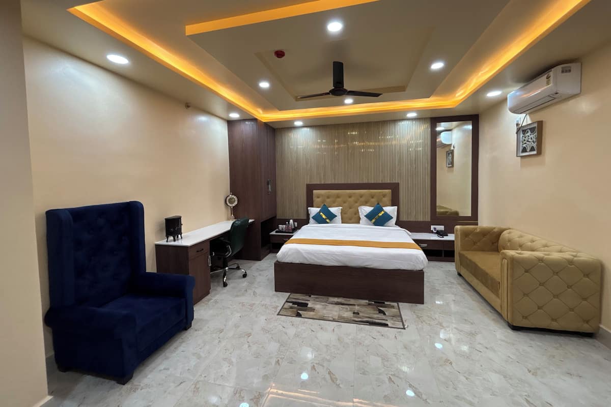 A modern hotel room with a large bed, a desk, a blue armchair, a sofa, and a ceiling fan.