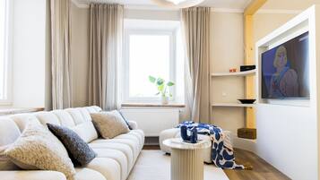 Ein Wohnzimmer mit einer Couch, einem Couchtisch, einem Fernseher und einem Fenster mit Vorhängen.