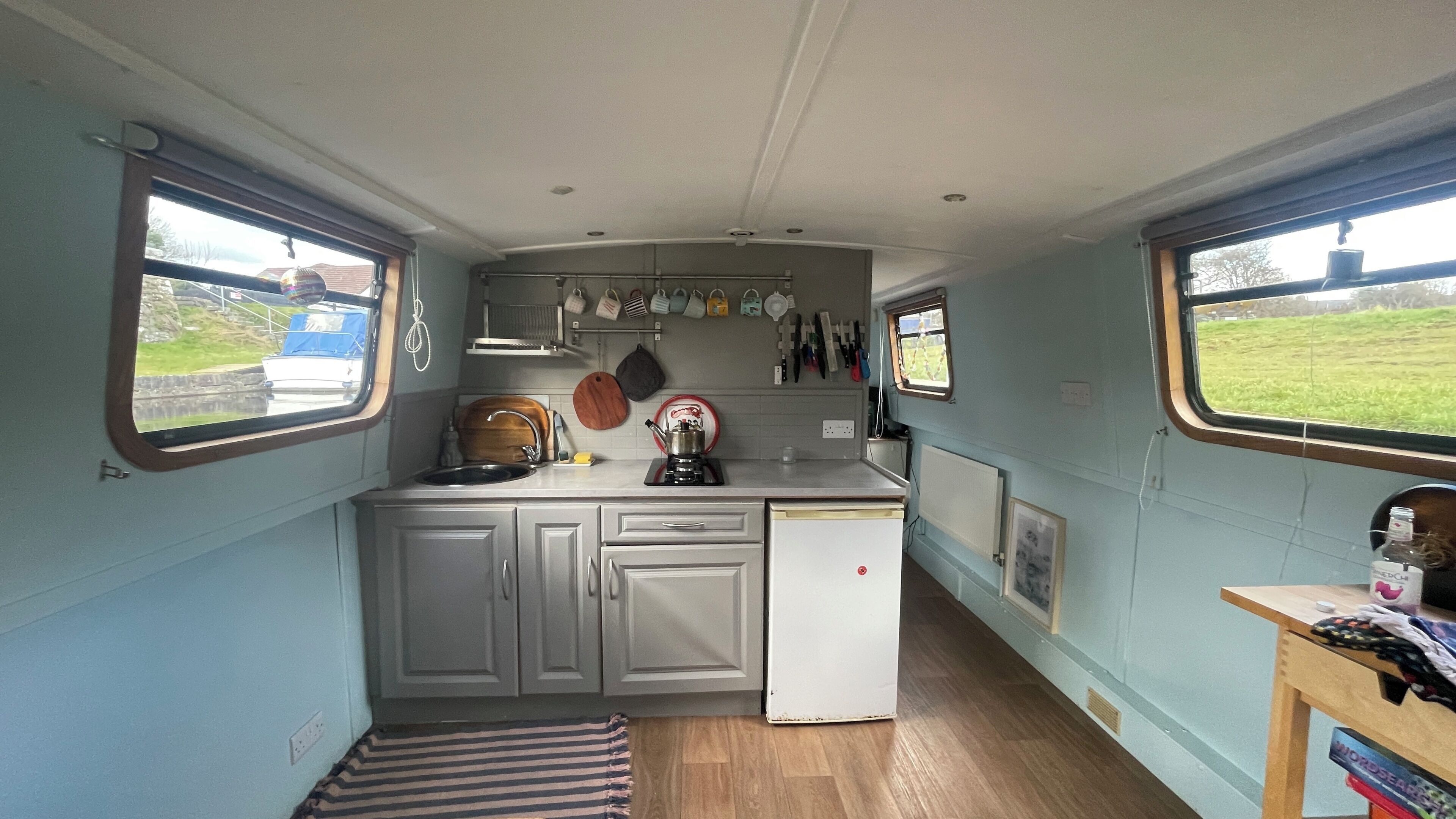A compact kitchen with a sink, a coffee machine, and a small refrigerator. There are cabinets and a window providing a view of the outside.