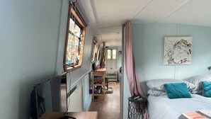 A narrow room with a bed, a TV, a wooden dresser, and a window with curtains.
