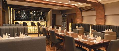 Un restaurante con una larga mesa de comedor, asientos acolchados y una zona de bar con estantes llenos de botellas.