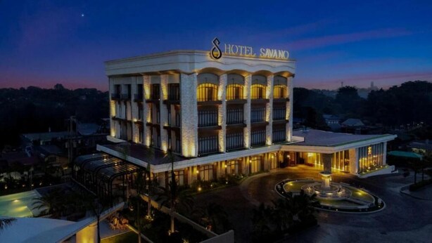 Un hotel de varios pisos con un letrero llamativo, un patio central y una zona ajardinada.