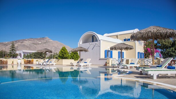 A clear blue pool with lounge chairs and umbrellas, surrounded by buildings with white and blue architecture. - Apartment Sea View BB 3 guests in a family hotel (Perivolos)